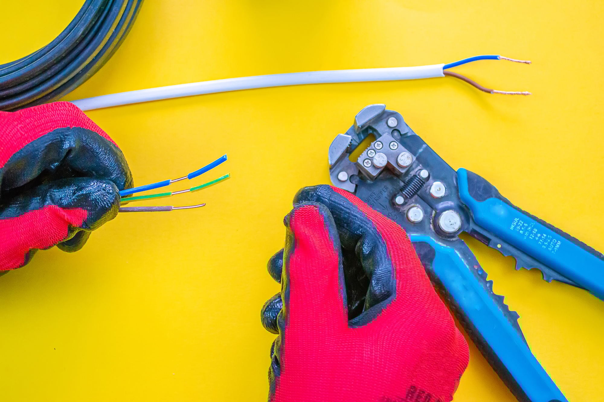 Electrician peeling off insulation from wires - closeup on hands and pliers.