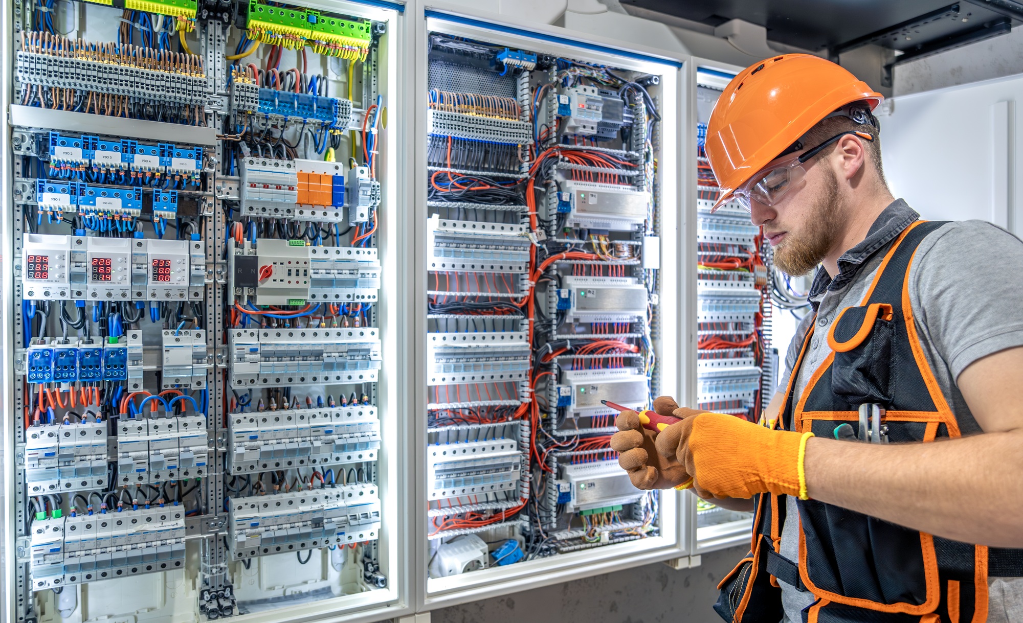 Male electrician working in electrical panel. Male electrician in overalls.